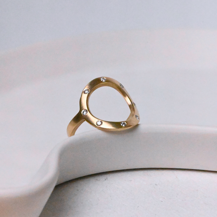 Gold open circle Sarin ring with 8 diamonds on a white ceramic dish
