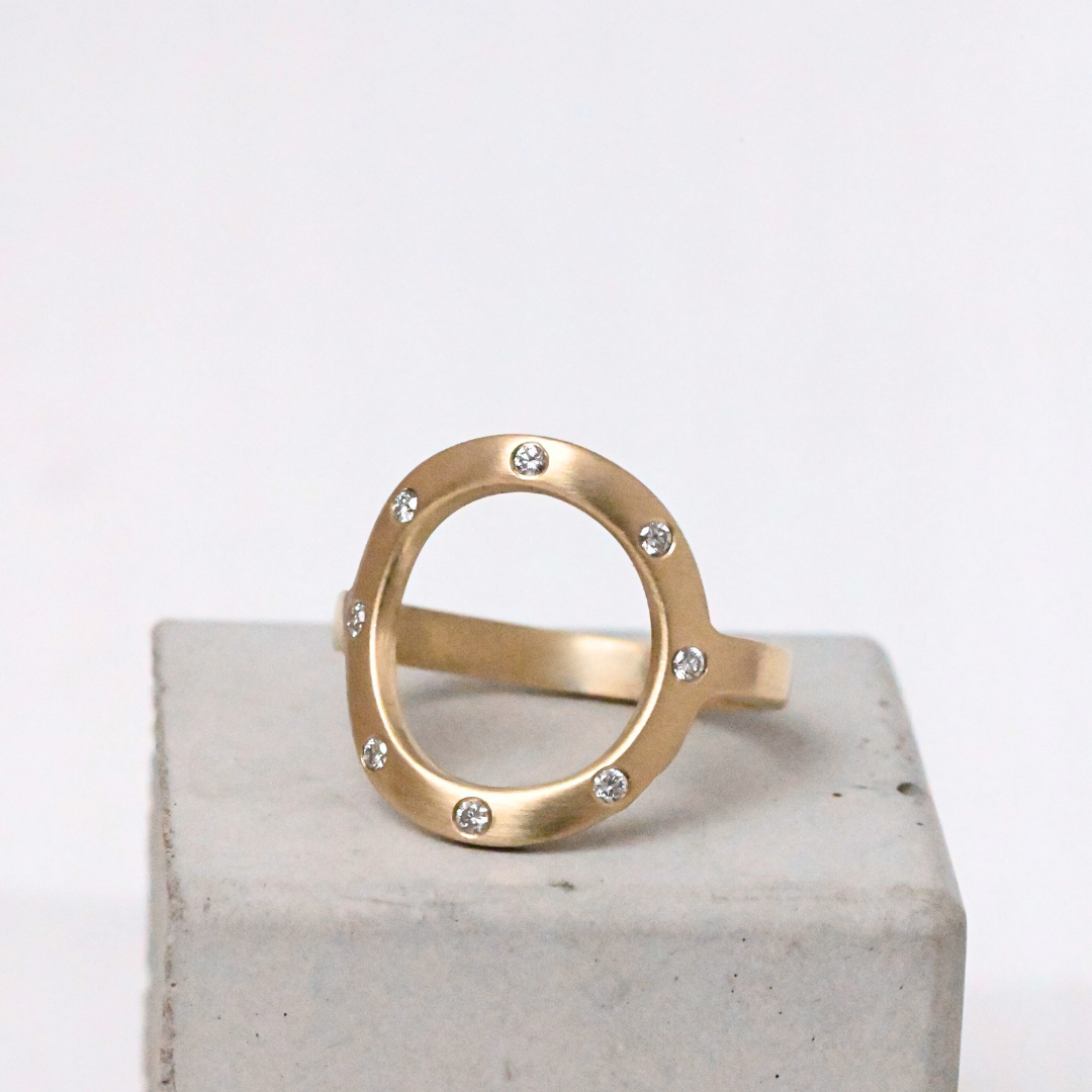 Gold open circle Sarin ring with 8 diamonds on a light gray background