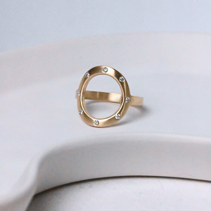 Gold open circle Sarin ring with 8 diamonds on a white ceramic surface