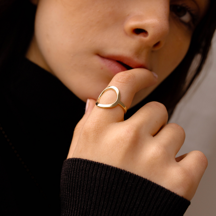 Close-up of a person wearing a gold open circle Sarin ring on their finger, with a blurred background.