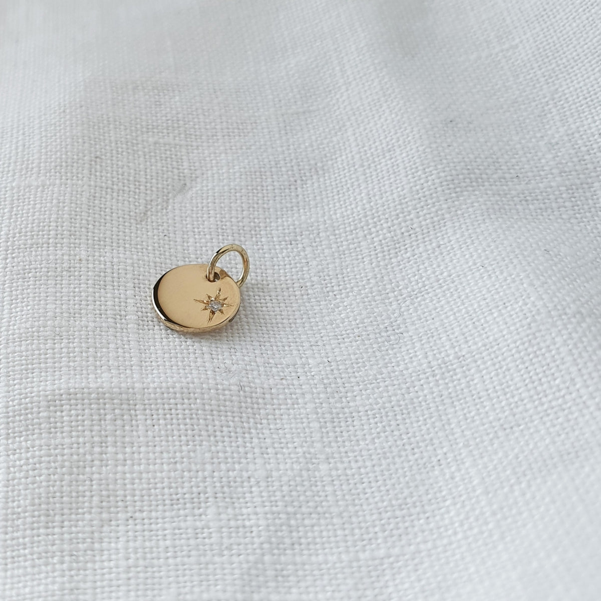 A solid gold pendant with a star set diamond on a white textured background.
