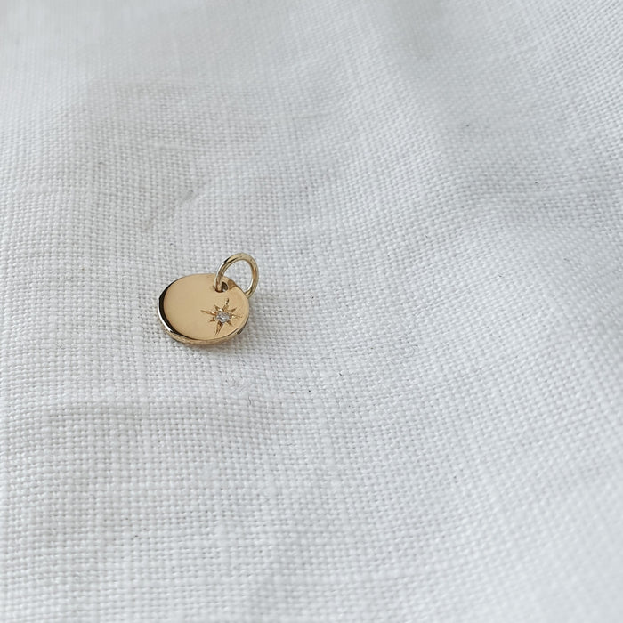 A solid gold pendant with a star set diamond on a white textured background.