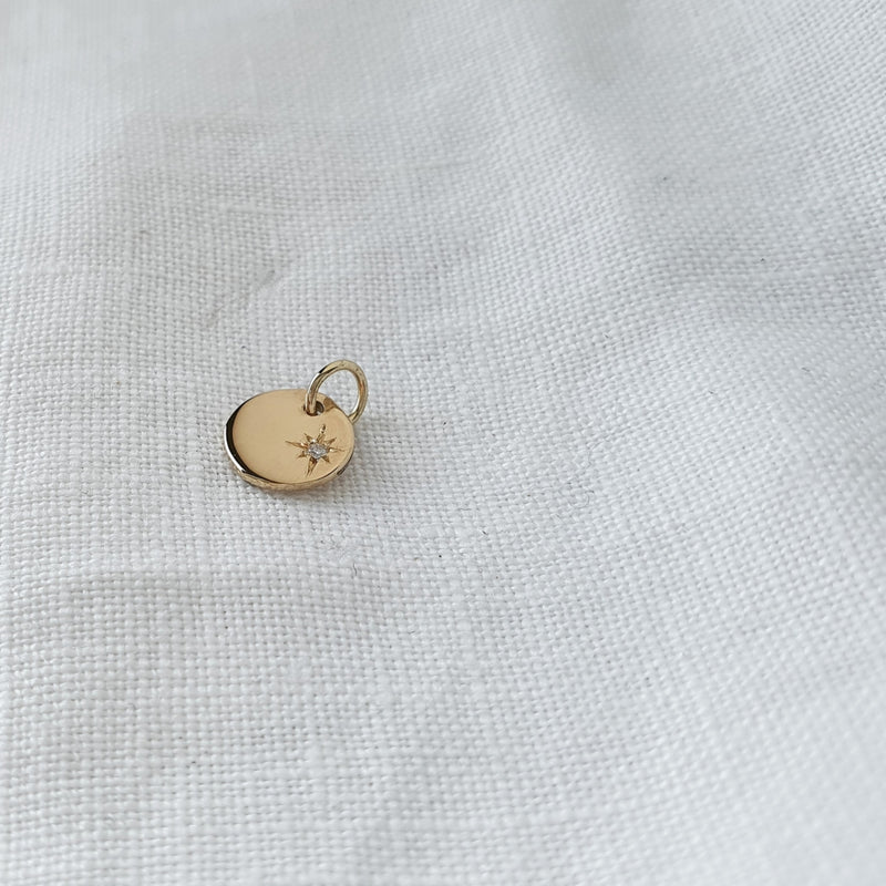 A solid gold pendant with a star set diamond on a white textured background.