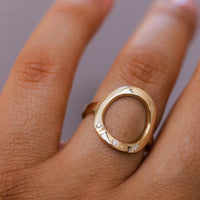 A gold open sarin ring with 3 diamonds  on a person's finger.