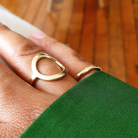 A gold open circle ring is displayed on a person's finger